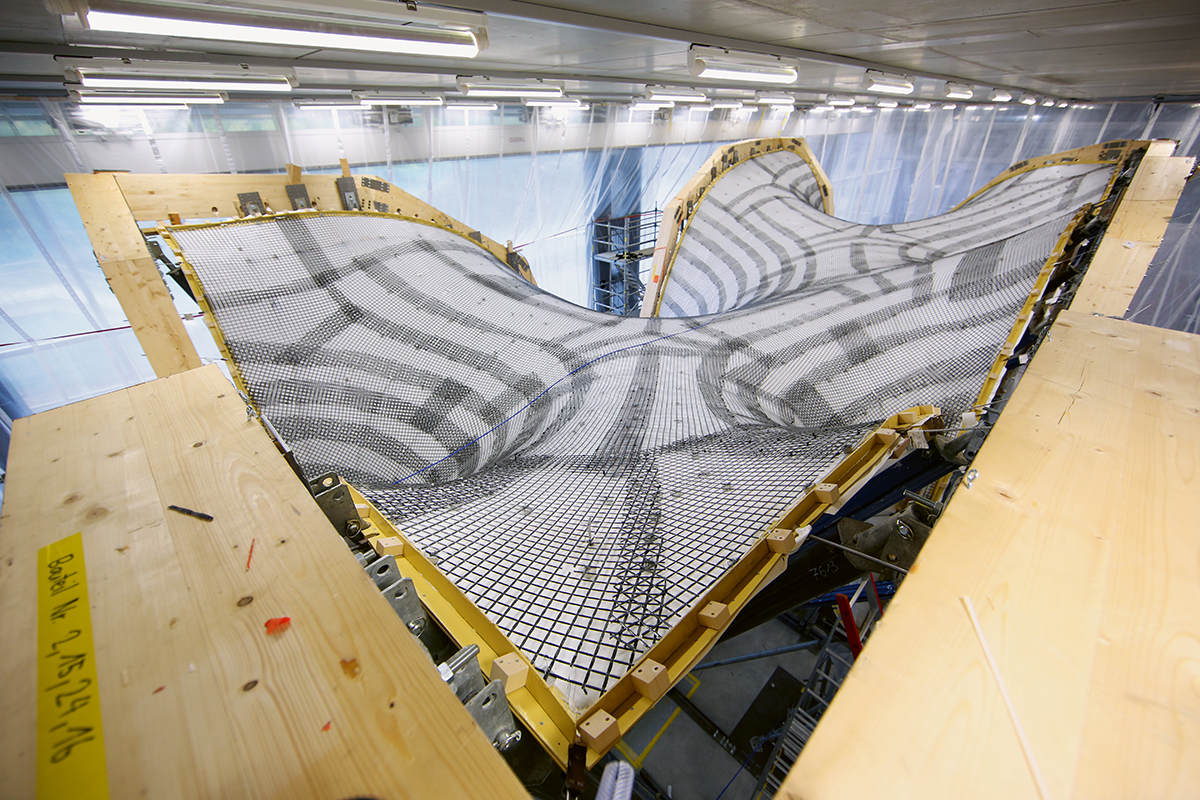 Dachschale vor dem Betonieren mit Überlappungen der Carbonbewehrung. Die Bewehrung ist an Abstandshaltern befestigt, die Teil der Verbindungsknoten des neuen Schalungssystem sind. Die Konstruktion ist an den umlaufenden Leimbindern aufgehängt und wird über daran befestigte Spannschlösser gespannt.