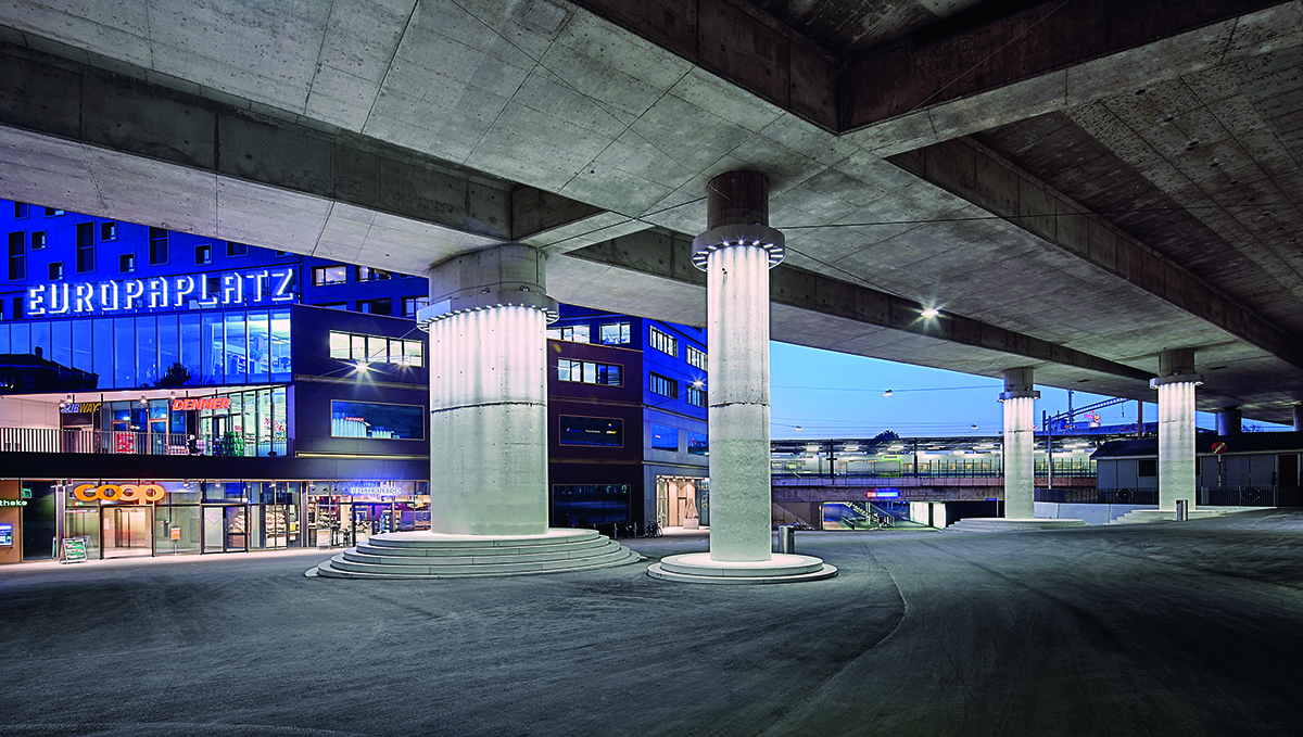 Pfeiler wandeln sich zu Säulen, der Beton löst sich auf in einen Lichtvorhang, der Asphalt wird zu einem Meer, das die Stützen umspült: In den Details liegt der Zauber der Aussenraumgestaltung am Europaplatz. Dank der Absenkung schliesst der Platz rundherum an den Bestand an.