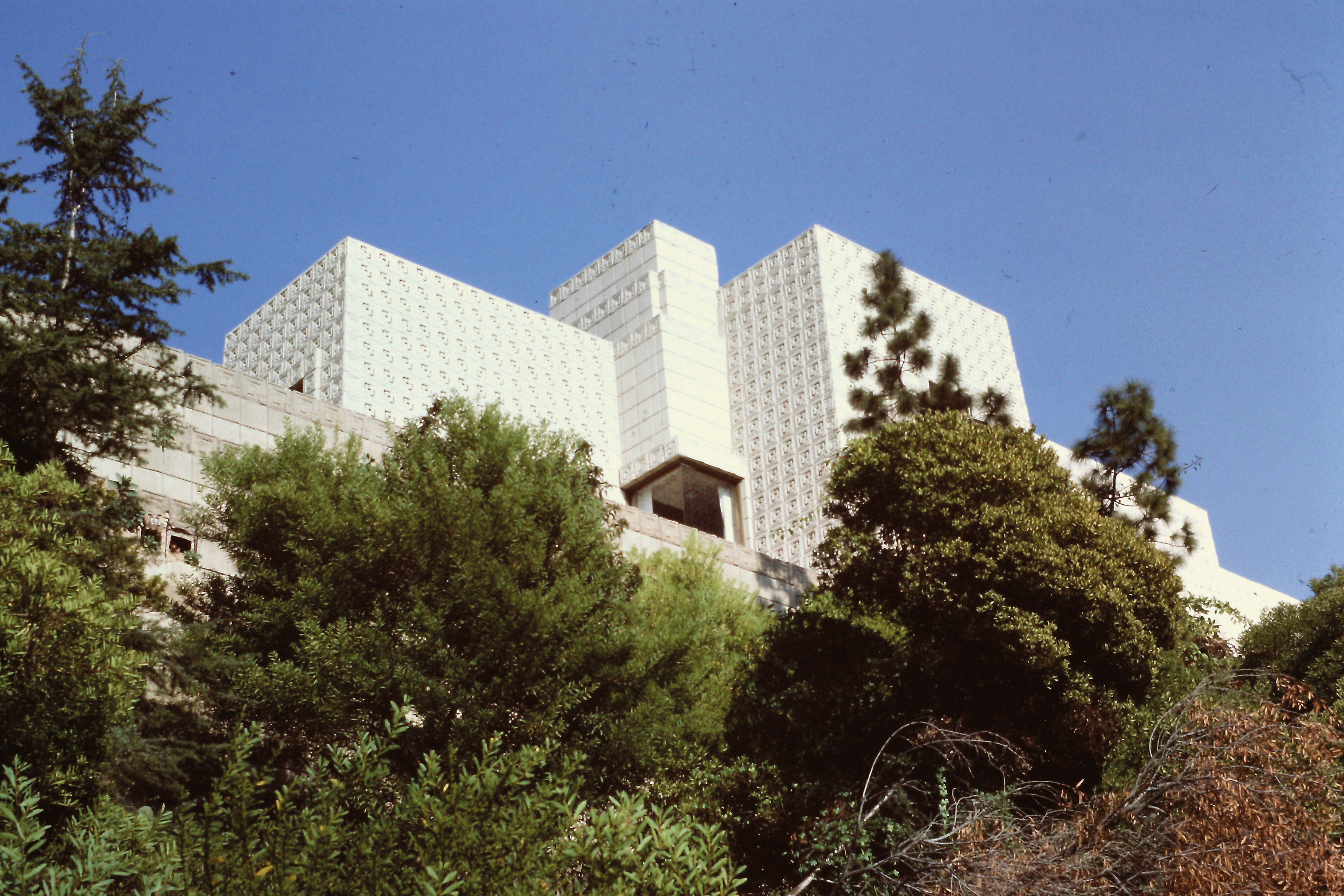 Carnet Amérique Dimanche 1er février 1987 « Ensuite, remontant Vermont jusqu’à Los Feliz et continuant dans Glendower Ave, à l’Ennis House, du même FLW, 1924, qui ne se voit que de l’extérieur. Entièrement revêtue d’une ‹ peau › décorative, la maison s’étale immensément sur une droite ; blanche, car il fait un soleil à pic, elle a des allures vaguement maya assez déplaisantes. La répétition obsessionnelle du carré de ciment (env. 30 cm de côté) estampé en fait une ‹ folie