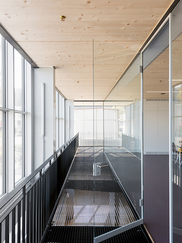 Im 1. OG führt fassadenseitig ein Gang entlang des Schulungsraums. Er lagert auf auskragenden Trägern, als Lauffläche dienen Gitterroste.