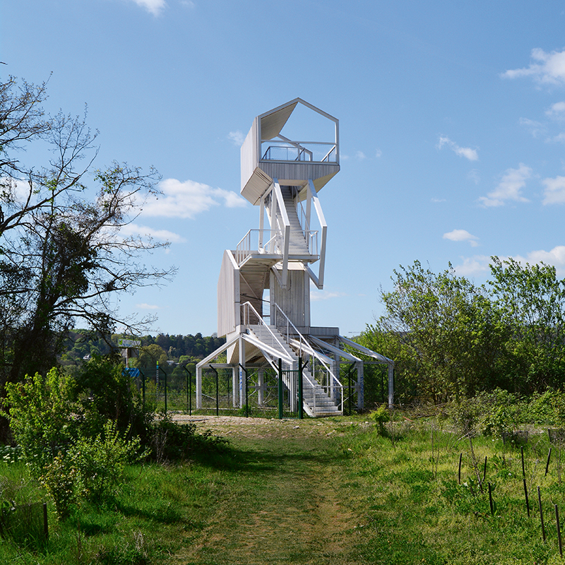 Der Aussichtsturm wirkt wie ein Gebilde aus übereinander­gestapelten Hausformen. Im unteren Bereich wurde er zum Schutz vor Vandalismus eingezäunt.