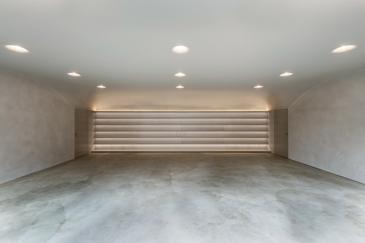 Die Akustikdecke ist von den hinteren Ecken ausgehend doppelt gewölbt und schafft einen schützenden Raum. Wände und Boden unterstützen mit den Spuren der Herstellung und den erdigen Farbtönen die angestrebte ruhige Atmosphäre. Ein Soundsystem funktioniert unsichtbar durch den Putz hindurch. Im wandfüllenden Regal können einzelne Muster zusammengestellt werden.