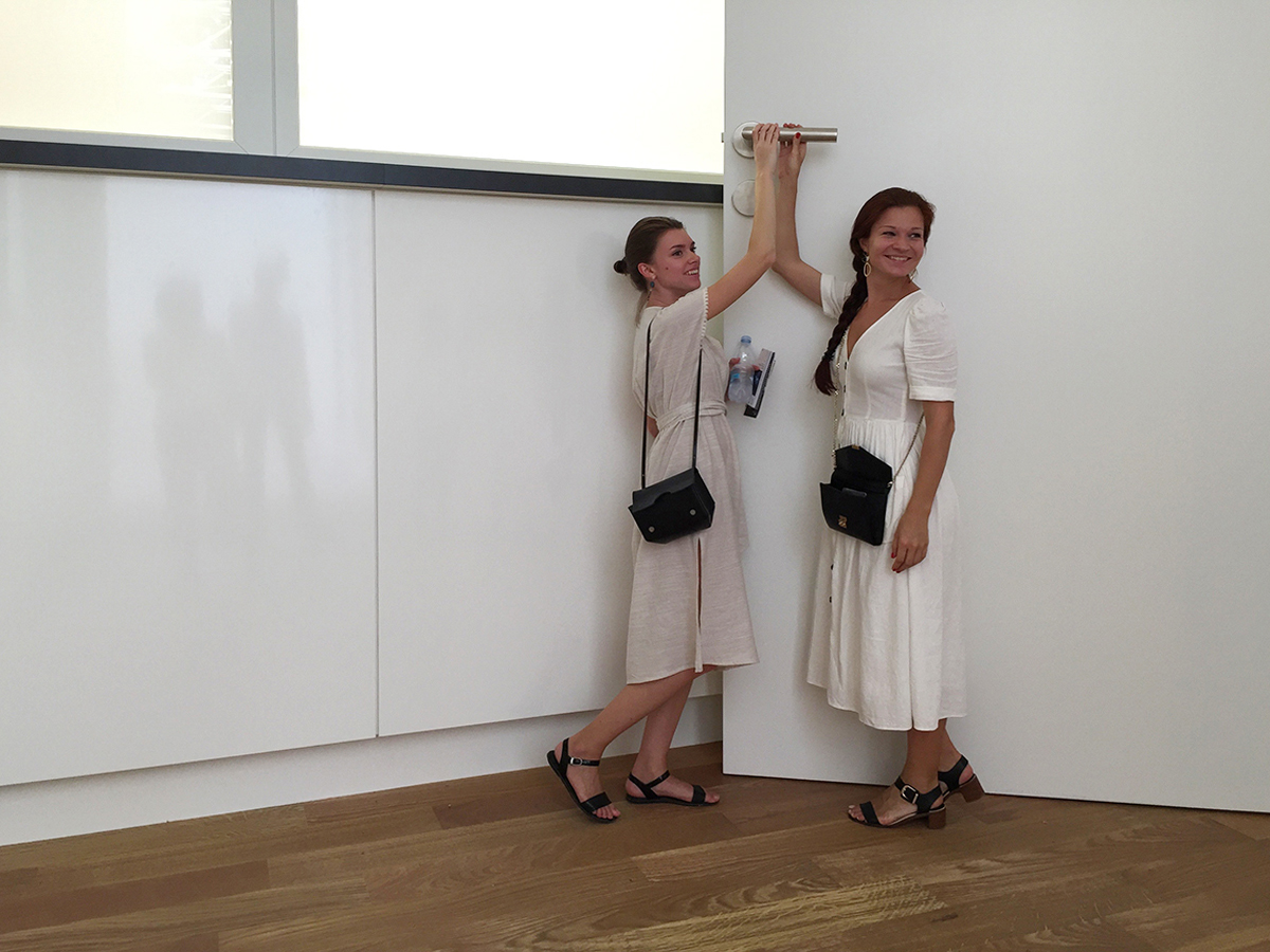 Zwei Besucherinnen lachen über die Türfalle über ihrem Kopf.