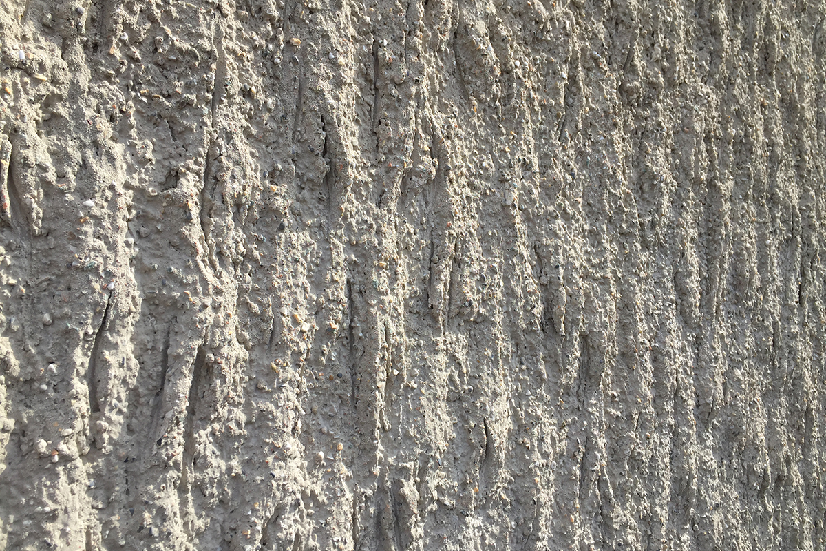 Im Streiflicht wirkt der modellierte Kellenwurfputz an der Aussenfassade wie eine Mondlandschaft. Der Ursprung des sandigen Materials ist ablesbar.