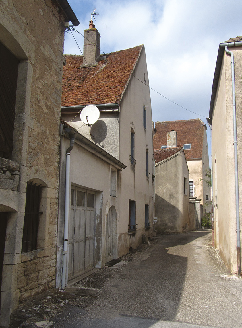 Maison Ducourtieux, avant. La maison située dans une rue étroite du village est constituée d’un corps de bâtiment principal à R+1 auquel est accolé un garage. Une terrasse a été aménagée sur son toit, accessible depuis le premier étage de la maison pour offrir un espace extérieur ouvert au sud, retrouver de la lumière et une vue dégagée