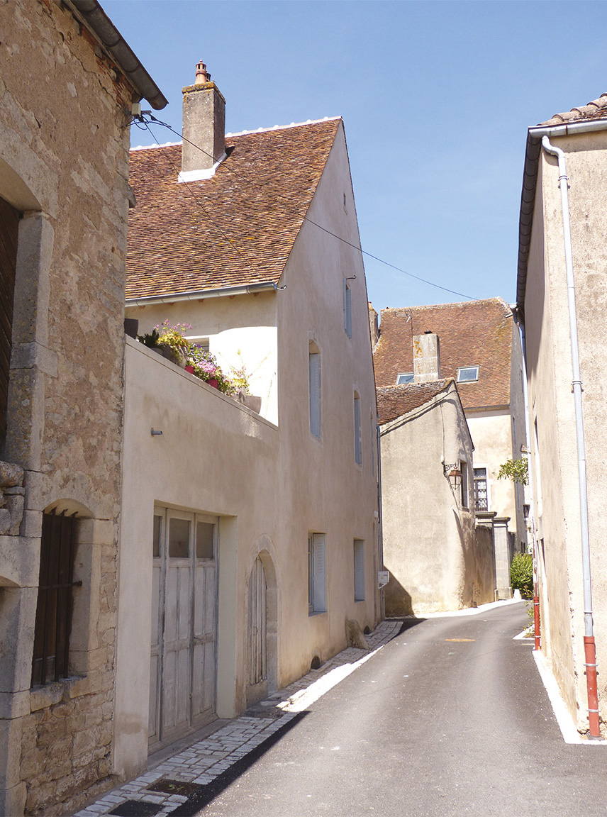 Maison Ducourtieux, après. La maison située dans une rue étroite du village est constituée d’un corps de bâtiment principal à R+1 auquel est accolé un garage. Une terrasse a été aménagée sur son toit, accessible depuis le premier étage de la maison pour offrir un espace extérieur ouvert au sud, retrouver de la lumière et une vue dégagée. (
