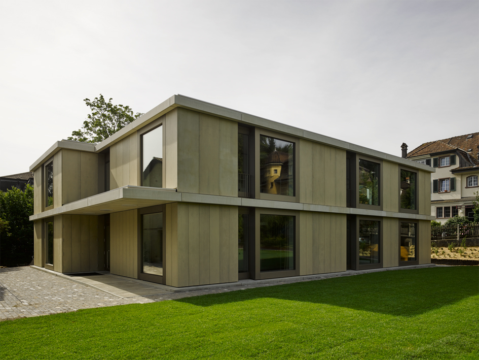 Markante Profilierungen und grosszügige Fensterflächen prägen das schlichte zweigeschossige Volumen.