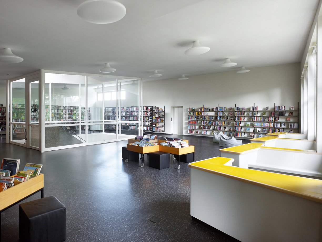 Im Obergeschoss von Trakt E ist neu die Gemeindebibliothek untergebracht. Sie wird über eine neue Treppe und über einen neu angebauten Liftturm erschlossen. Die Sitzkojen entlang der Fenster sind ein Entwurf der Architekten.