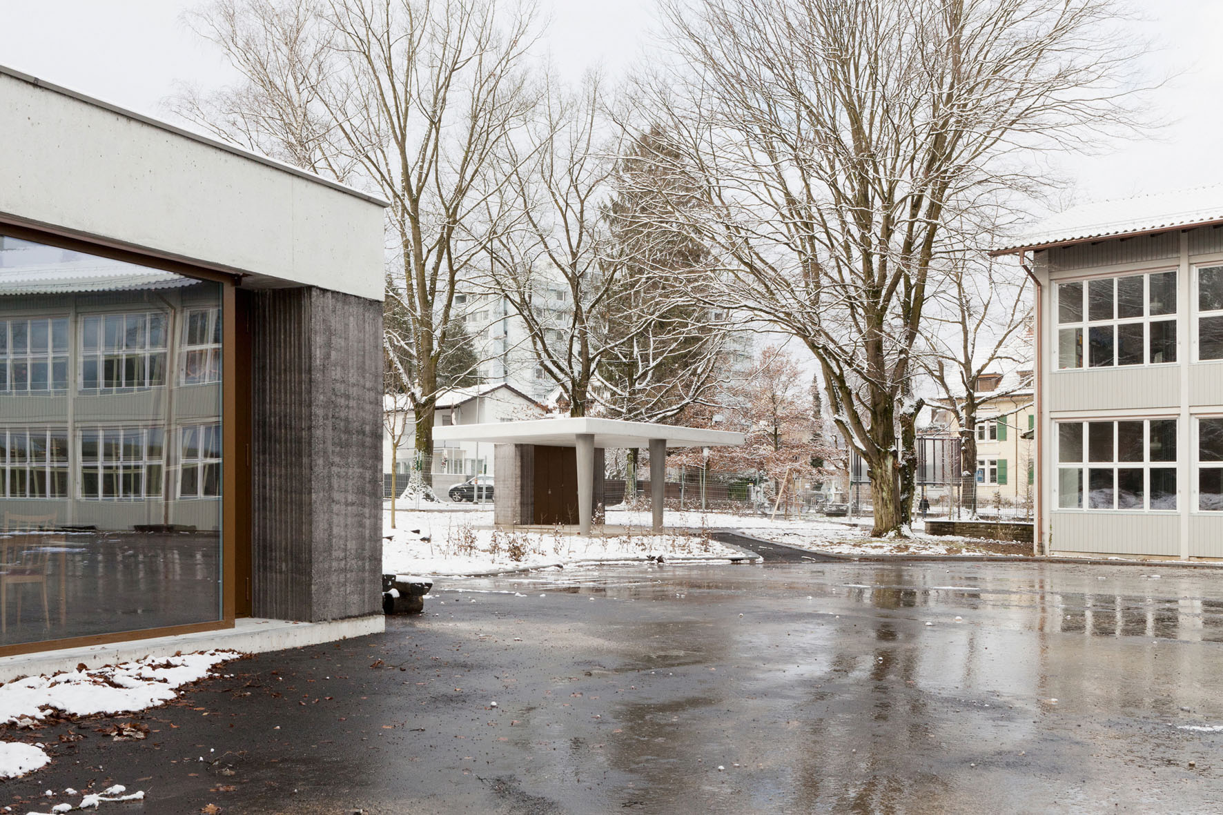 Gruppenraum und Pausenunterstand mit Klassentrakt. Die beiden Gruppenräume öffnen sich zu den Schulhöfen. In der Oberfläche der gestampften Elemente zeichnen sich die schräg angeordneten Latten der Schalung ab