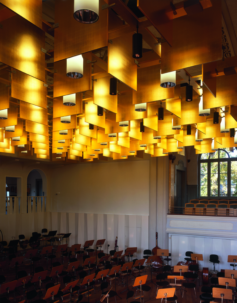 Bühnenbereich der Tonhalle St. Gallen mit dem unter der Decke aufgehängten Schalldiffraktor. Hinter der Bühne sind die schalldiffundierende weisse Holzverkleidung und die Holzbalustrade der Empore mit dem gleichen Zweck erkennbar. Die Bühne ist für ein Or