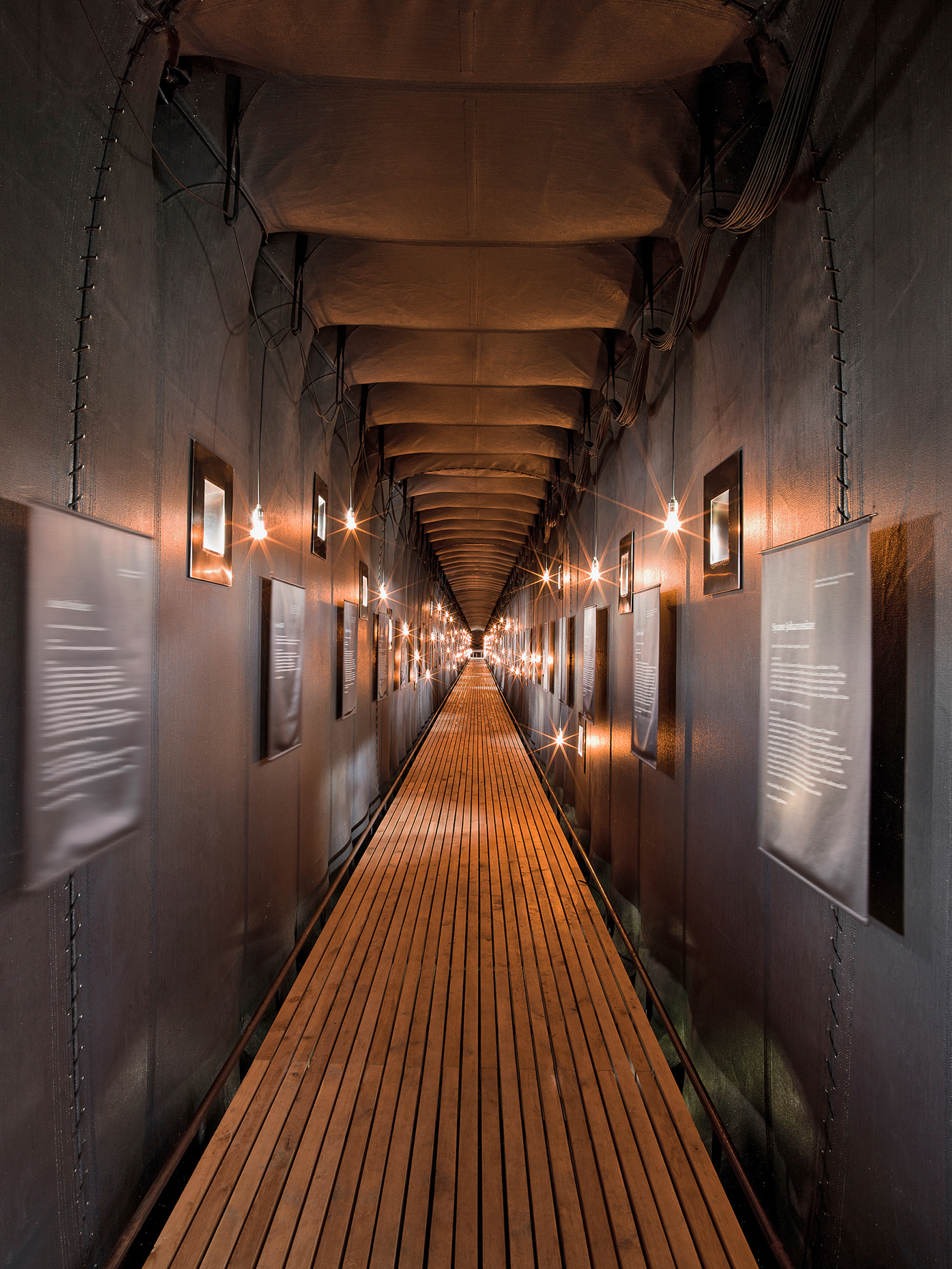 Blick in die Ausstellung. Ein Licht und ein Fenster für jedes der 91 Opfer, dazu die Namen, Lebensdaten und Auszüge aus den Prozessakten. Die Öffnungen sind in unregelmässigen Abständen und in sechs unterschiedlichen Höhen angeordnet.