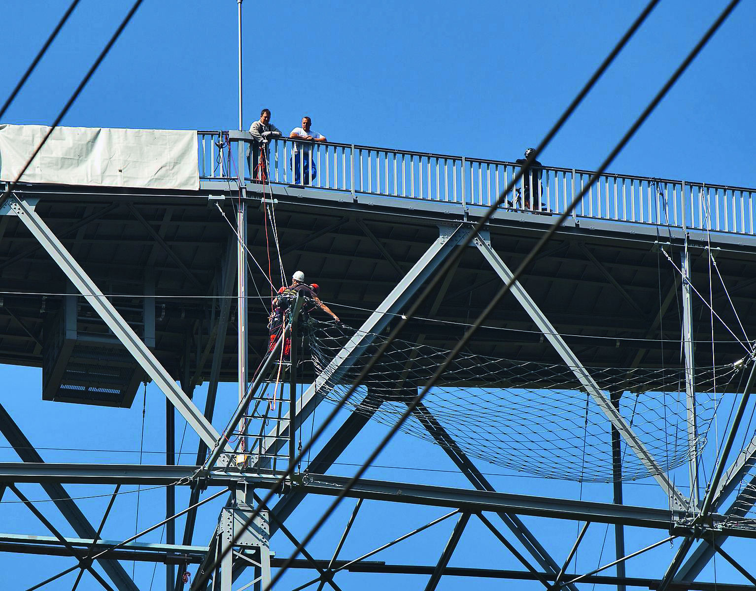 Die Haggenbrücke nach der Instandsetzung mit neuer, orthotroper Stahlplatte. Der «Stahlkäfig» unter der Fahrbahnplatte nimmt die Schwingungsdämpfer auf. Fachkräfte bringen die Suizidpräventionsnetze an. Eine zusätzliche Gefahr sind die Hochspannungsleitungen unter der Brücke